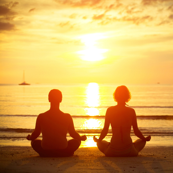A couple enjoying a yoga meetup on the beach. Invite your friends to meditate and relax on buddypassgo.com! 